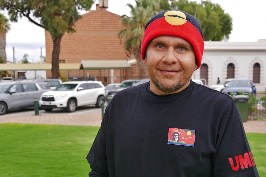 An indigenous man wearing a black shirt and an aboriginal flag themed beanie 
