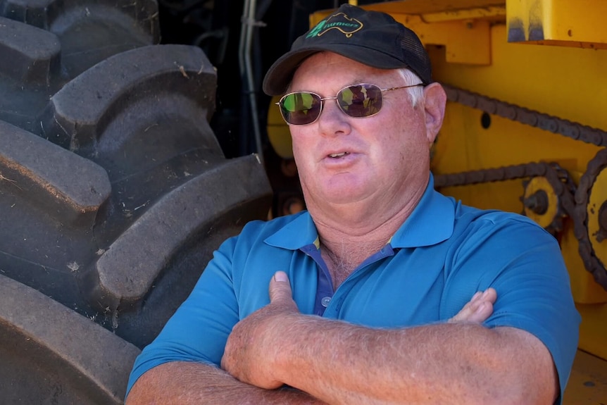 A man in workwear and sunglasses standing in front of a tractor