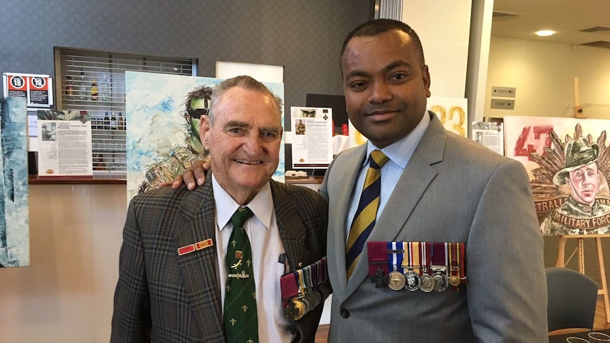 Two men stand with their arms around each other and with medals displayed on their jackets.