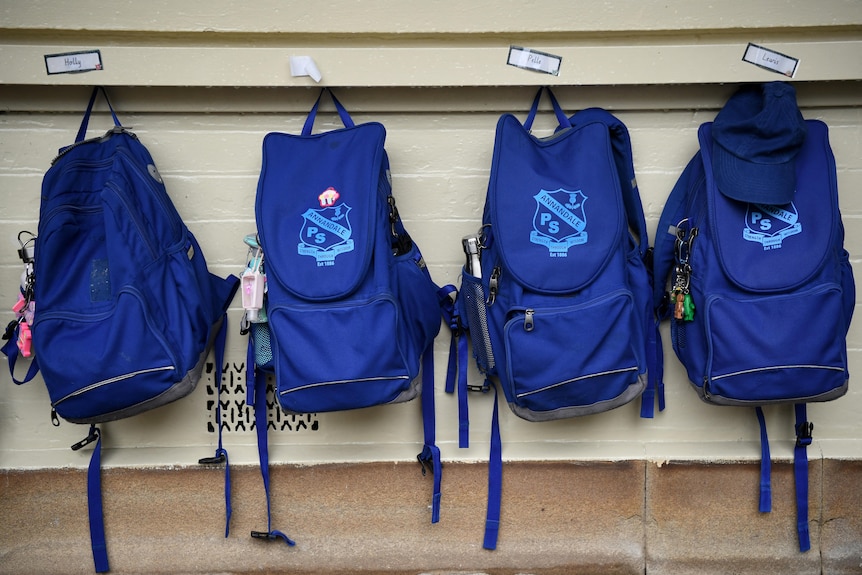 school backpacks hang off hooks outside a classroom