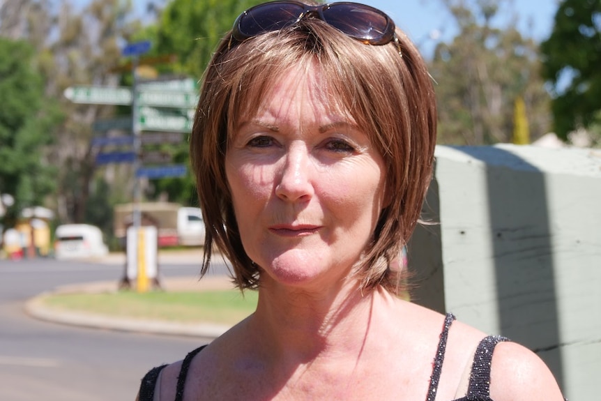 A middle aged woman with sunnies on her head looks at the camera with a serious expression.