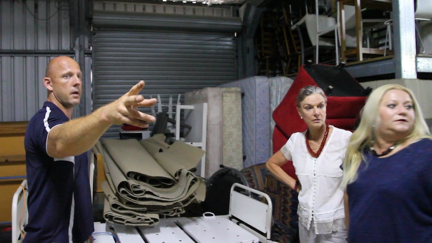 Man points at something that two women are looking at inside a storage shed.