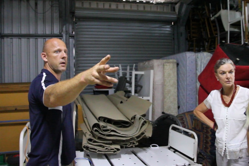 Man points at something that two women are looking at inside a storage shed.