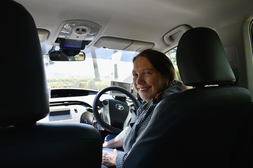 A woman sitting in the driver's seat of a taxi, smiling.