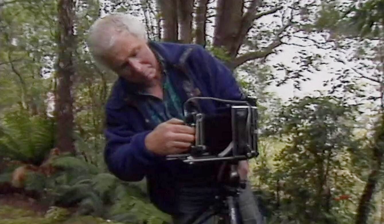 Peter Dombrovskis adjusting his camera amidst a bush setting.