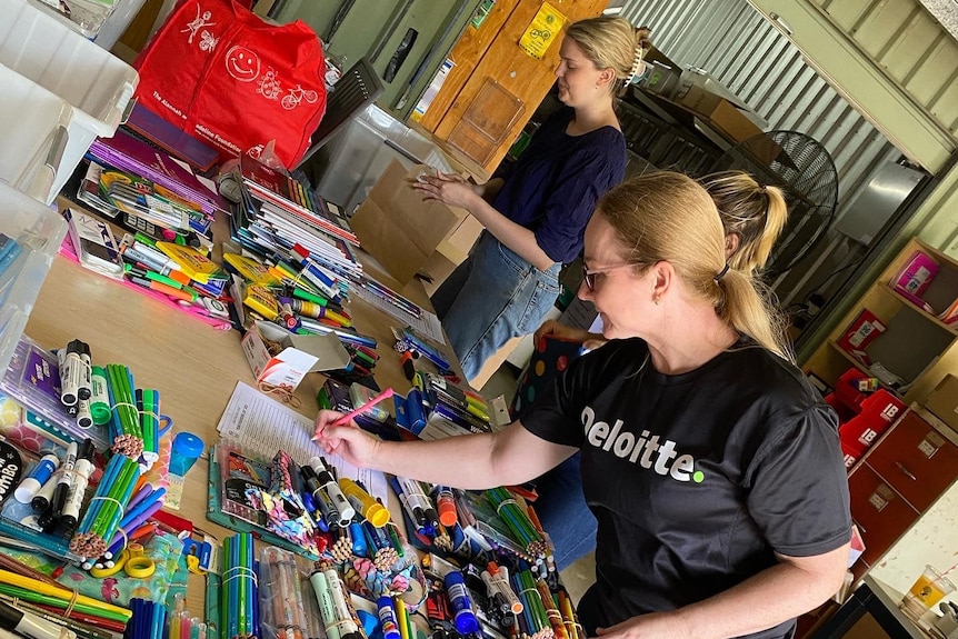 Two ladies standing at a table sorting out stationery supplies.