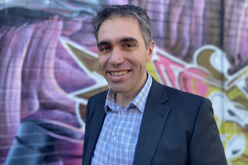 Elio D'Amato stands against a graffiti covered wall. 