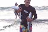 A man walks out of the surf carrying two wild salmon.