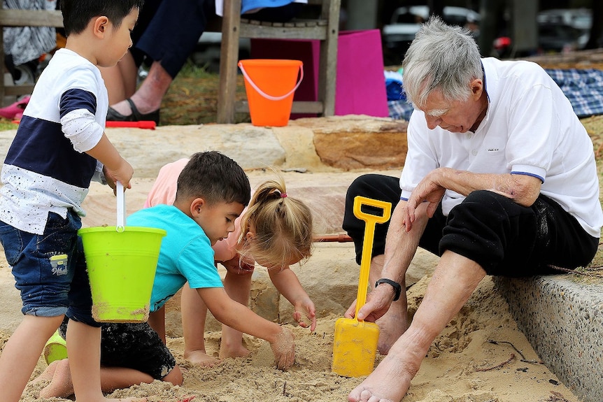 An elderly man plays in a sandpit with three children on the ABC TV series Old People's Home For 4 Year Olds.