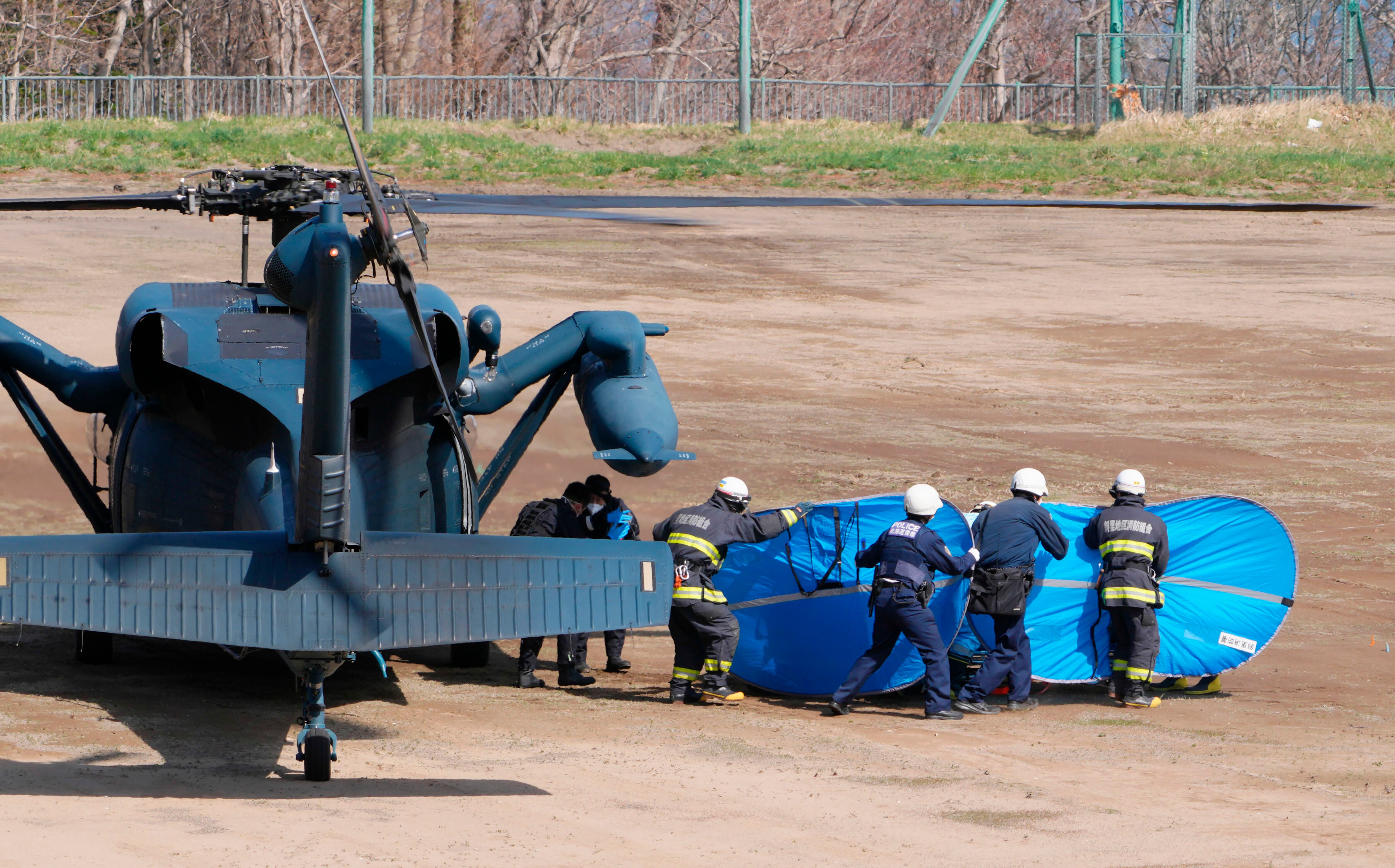 Four firefighters carry a blue bag next to a heclicopter.