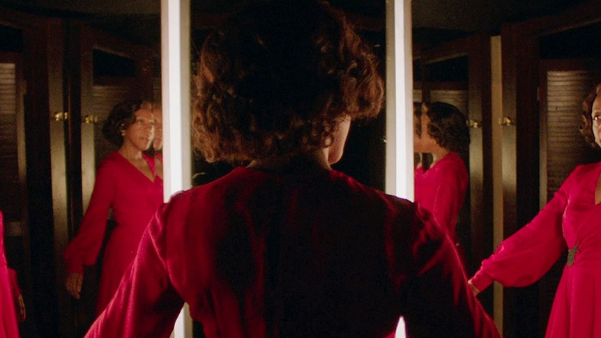 A women in a red dress stands in front of a semicircle of mirrors