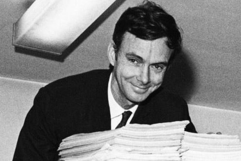 A black and white photo of a man leaning over a pile of papers