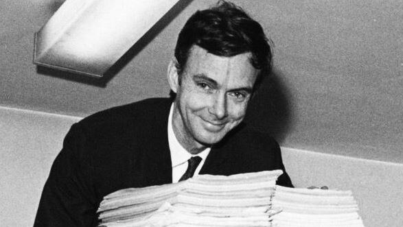 A black and white photo of a man leaning over a pile of papers