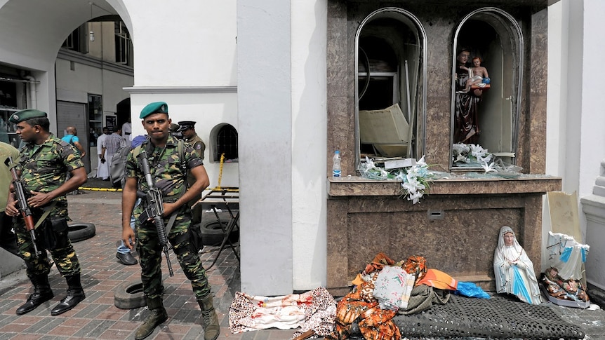 Soldiers guard a destroyed religious shrine, with a statue split in half among debris on the ground