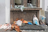 Soldiers guard a destroyed religious shrine, with a statue split in half among debris on the ground