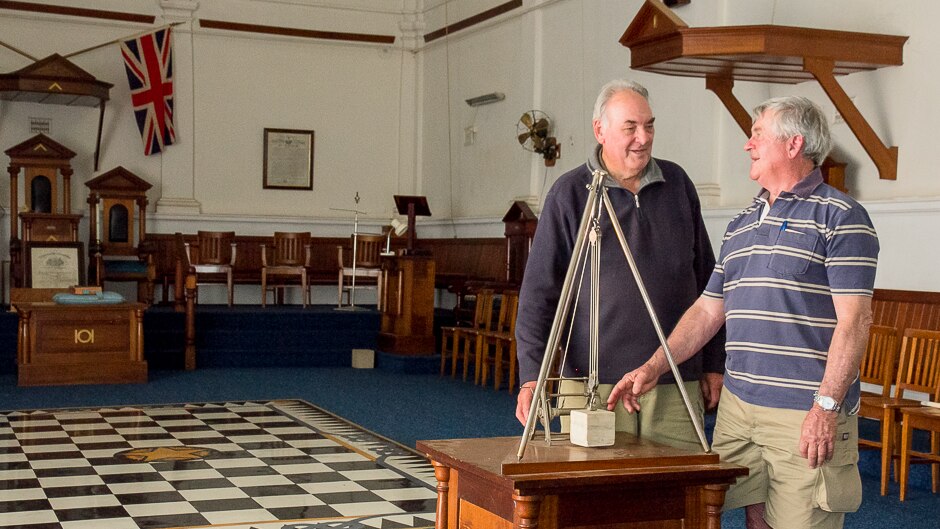 Two men stand masonic equipment inside a masonic lodge complete with chequerboard floor