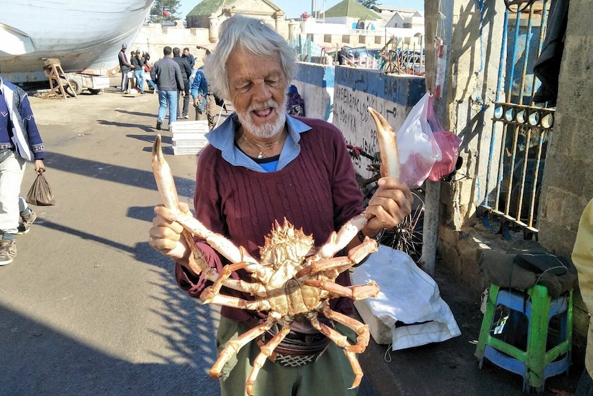 a man stands looking down at the huge crab he's holding 