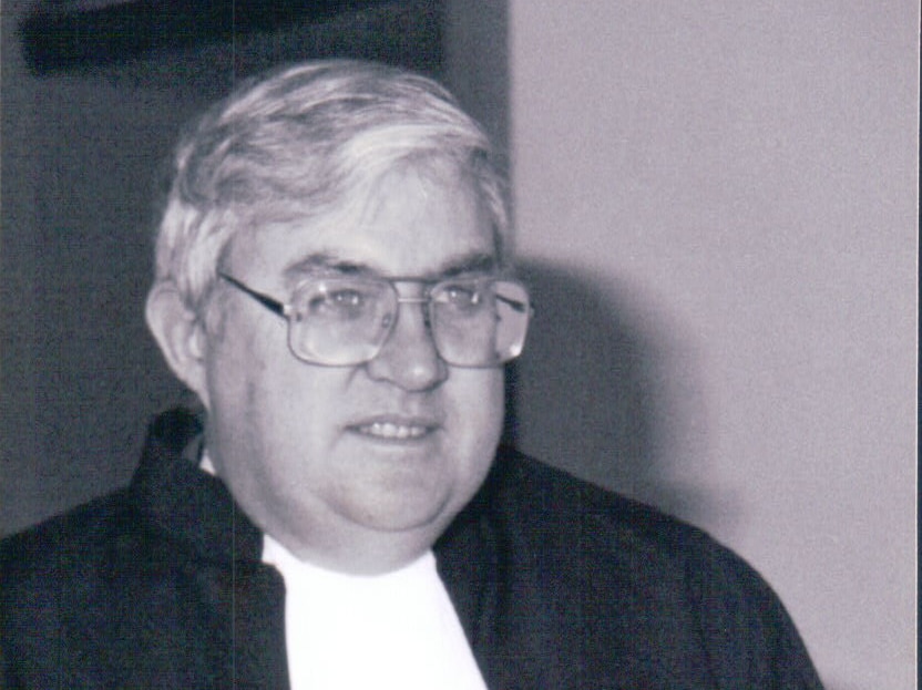 A black and white photo of a man with thick glasses in a lawyer's robe
