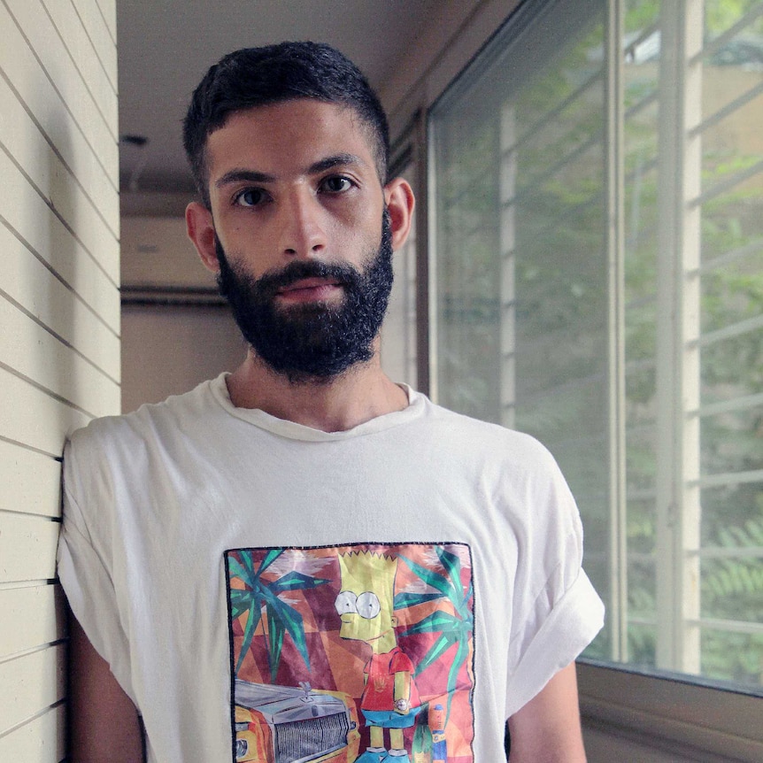 A young man leaning against a wall in a Bart Simpson t-shirt