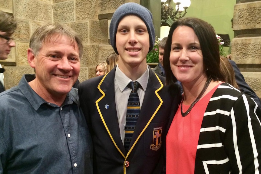 A student in a school blazer and beanie flanked by his parents.