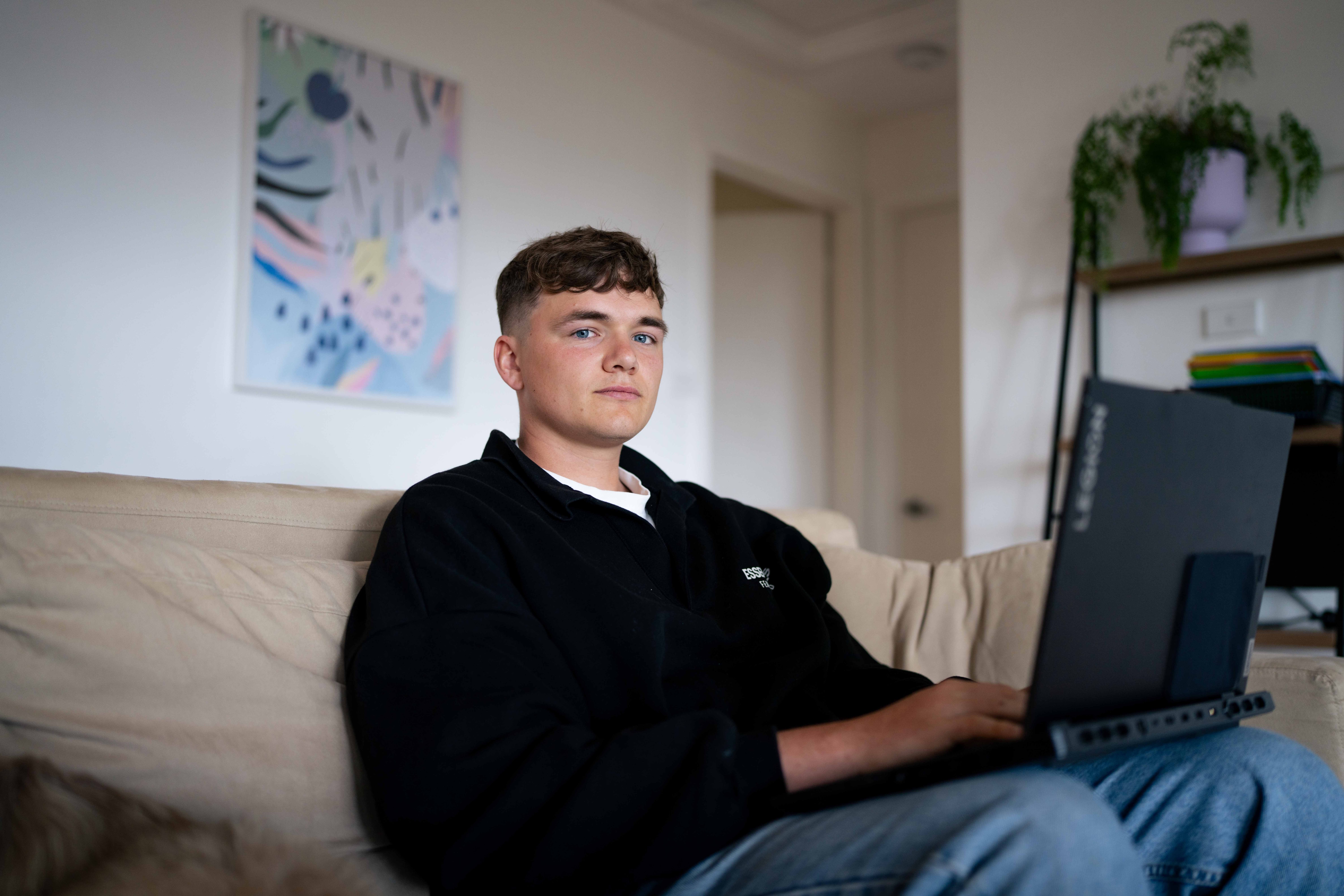 Man sits on couch with a laptop resting on his lap, posing for photo