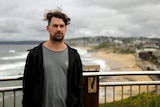 A windswept man in a hoodie poses on a bluff above a beach