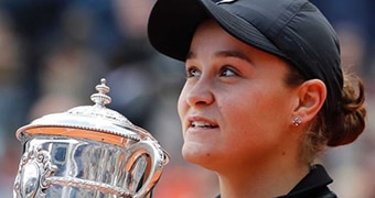 Close-up of woman wearing black cap holding large silver trophy, and looking up towards sky.