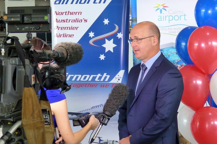 A man talks to a news crew in front of an Airnorth banner.