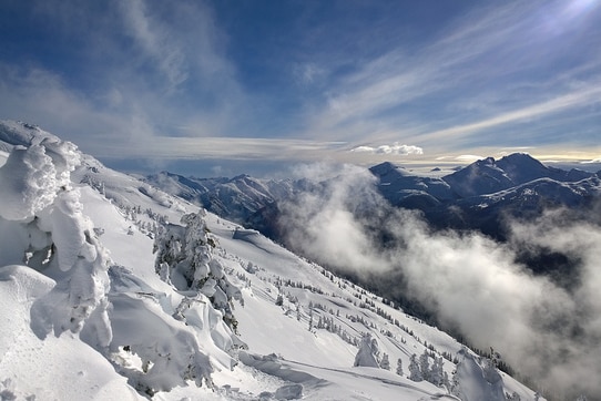 Mountains covered in fresh show with trees poking through the snow and blue skies above