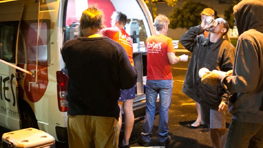 Four homeless men and two volunteers standing behind van