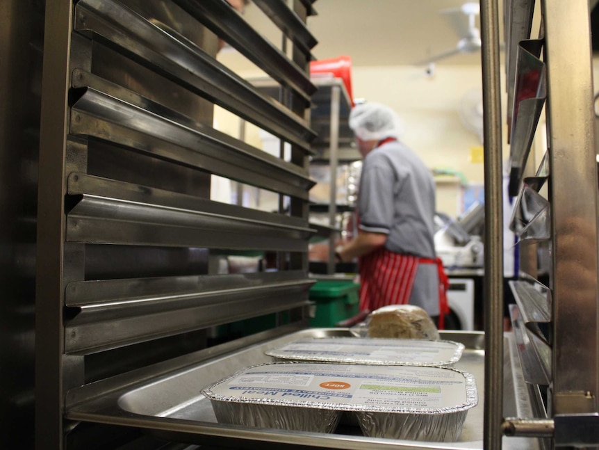 Close up image of a kitchen tray on a rack with a man in a hairnet in the background.