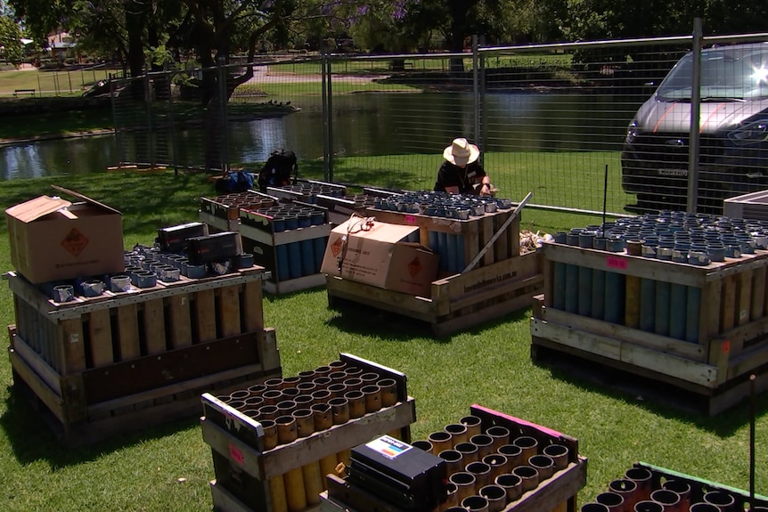 A man with boxes and pallets of fireworks near a lake
