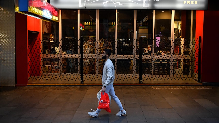 一个人拿着购物袋走在街上，经过一家关门的纪念品店。