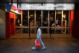 A man walks down the street with a shopping bag, passed a shuttered souvenir shop.