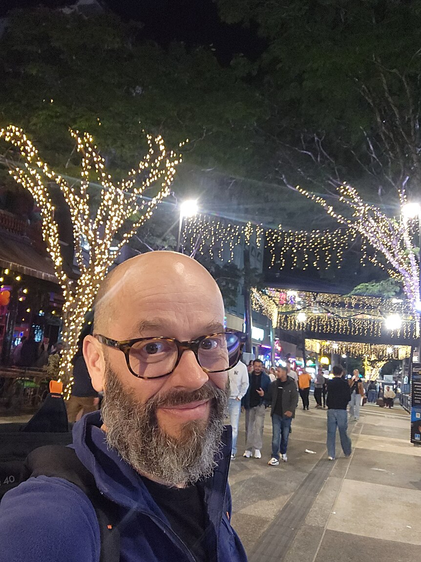 selfie of Simon Austin, a bald man with a beard, standing outside in the Brunswick St Mall in Brisbane