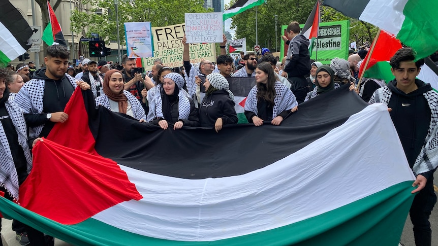 People holding a Palestinian flag at the front of a march through Melbourne.