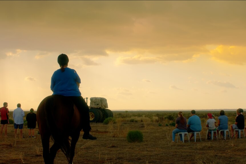 A person rides a horse in a paddock at dusk.