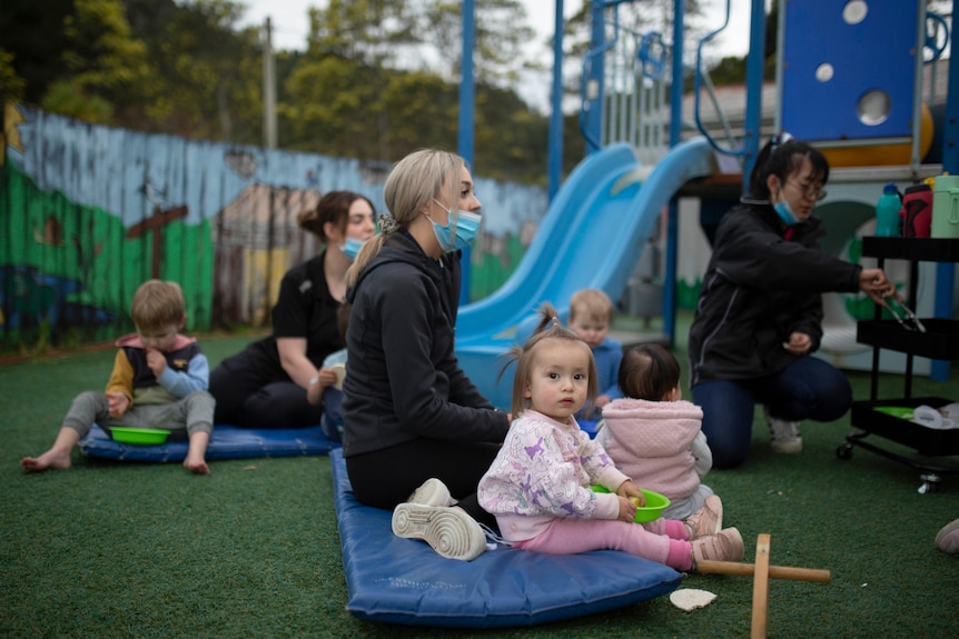 Staff sit with children in the playground of a childcare centre