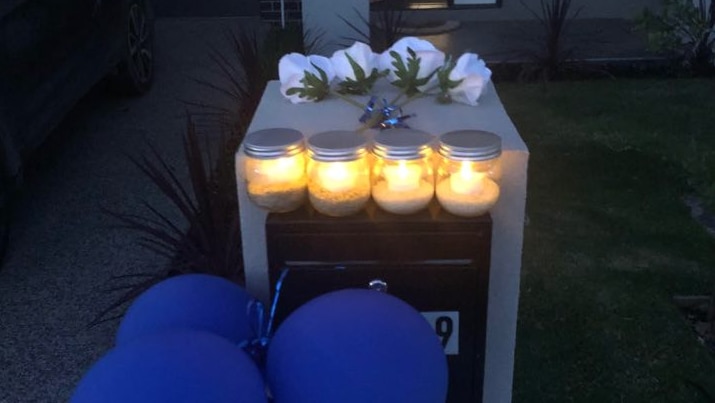 Four white roses and four candles are placed on the letterbox out the front of a suburban home.