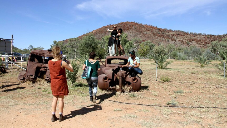 Tourists pose on top of burned out car in front of East MacDonnell Ranges