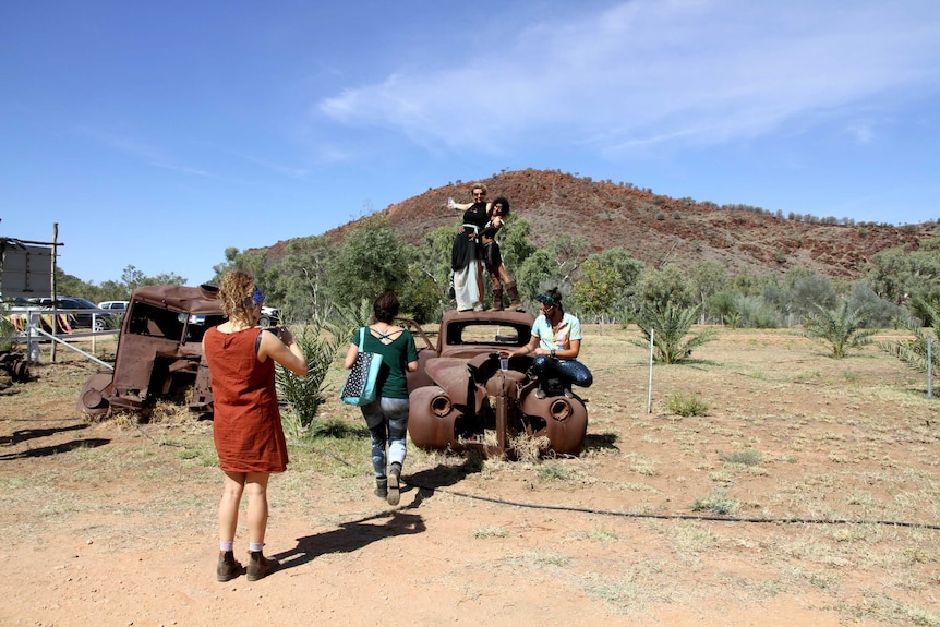 Tourists pose on top of burned out car in front of East MacDonnell Ranges