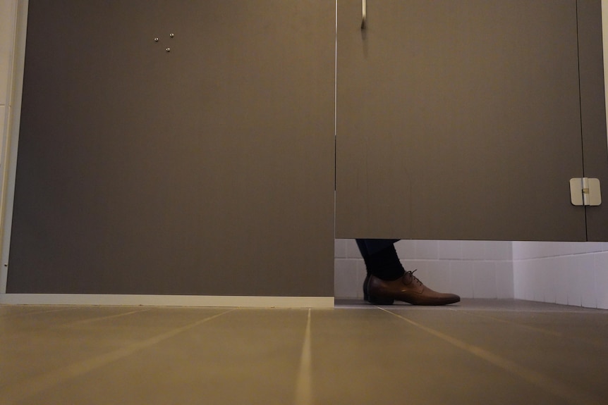 A man's business shoes show underneath a toilet cubicle