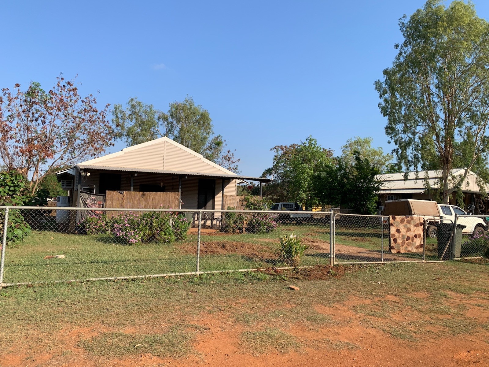 A house behind a low-fence, dirt and grass, car parked in front yard.
