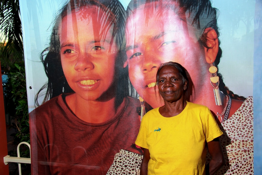 A lady stands next to a large photograph of two young girls. 