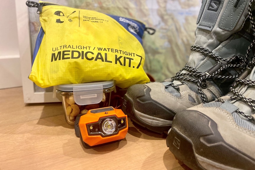 Blue hiking shoes, an orange head torch, a yellow medical kit and a container of nuts in front of a map