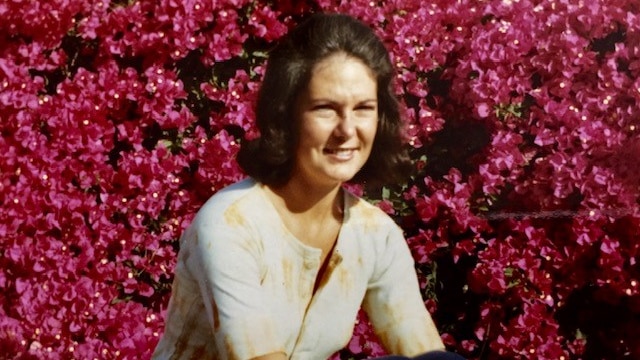 A woman sits in a field of bright pink flowers, looking away from the camera.