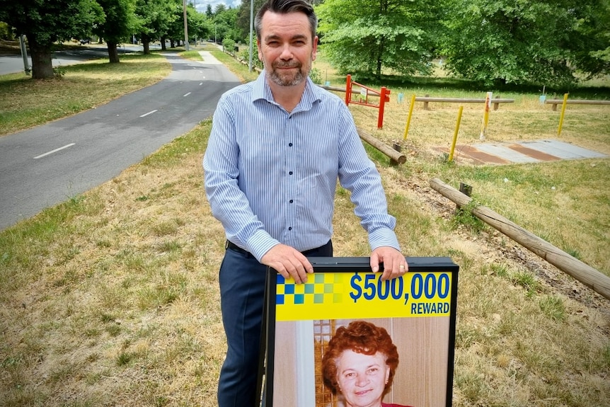 A man in a shirt stands behind a corflute with an image of an older woman.