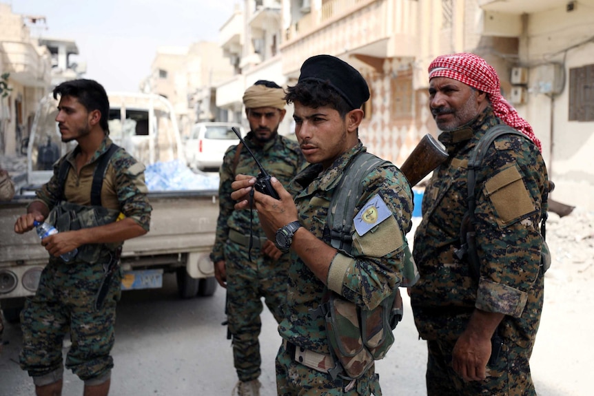 Four fighters from the Syrian Democratic Forces stand on a run-down street in Raqqa.