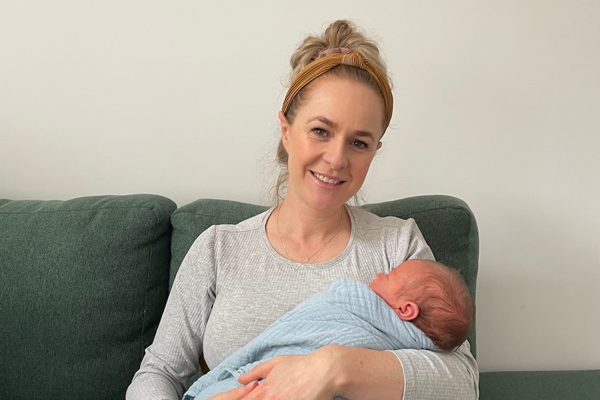 Young mum holds her newborn baby in arms and smiles.