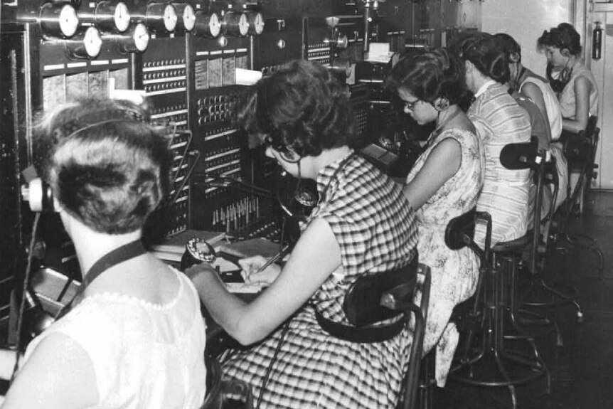 A photo from 1958 showing a row of women wearing headsets, seated before a large manual telephone exchange